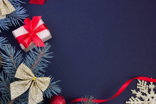Fondo elegante de Navidad con un lugar para una inscripción, juguetes de Navidad y ramas de un árbol de Navidad sobre un fondo oscuro en los bordes, un regalo con una cinta roja. — Foto de Stock