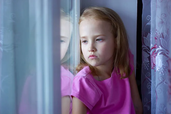 Ledsen flicka i rosa klänning sitter vid fönstret, ensamhet koncept, isolering Stockfoto