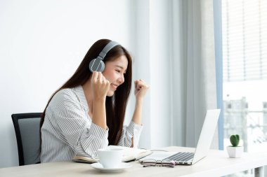 Video çağrısı, kulaklık takan genç bir Asyalı kadın, internetteki uzun mesafeli video ile iletişim kuruyor, dijital laptop ekranına bakıyor, bir arkadaşıyla mutlu bir şekilde selamlaşıyor..