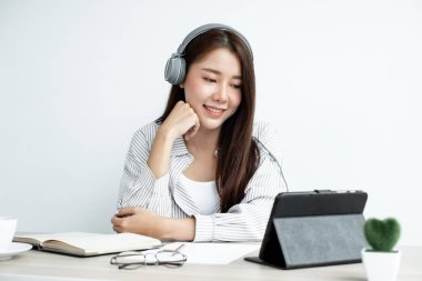 Kulaklık takan genç bir Asyalı kadını ararken dijital tabletteki internet üzerinden arkadaşlarıyla mutlu bir şekilde iletişim kuruyor..