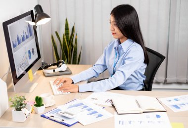 Ofiste çalışırken mutlu ve neşeli bir gülümsemeyle dizüstü bilgisayarda çalışan Asyalı kadın..