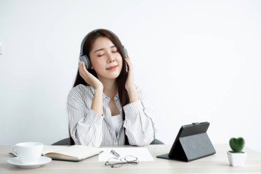 Kulaklık takan genç bir Asyalı kadını ararken dijital tabletteki internet üzerinden arkadaşlarıyla mutlu bir şekilde iletişim kuruyor..