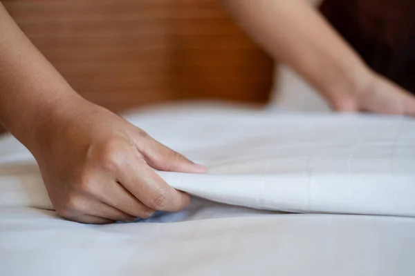 The hotel maid cleans and makes the bed in the hotel room.