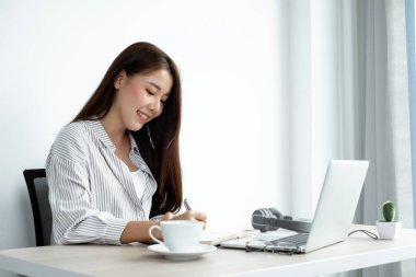 Asyalı kız üniversite öğrencileri evde ders çalışıyor, ekstra dersler alıyor, videolar izliyor ve dijital bir laptoptan not alıyor, evde bir masada otururken ekrana bakarak ödev yapıyor..