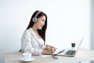 Kulaklık takan Asyalı bayan üniversite öğrencisi online ders vermeyi, video izlemeyi ve dijital tabletten not almayı ya da evde otururken ekrana bakarak ödev yapmayı seviyor..