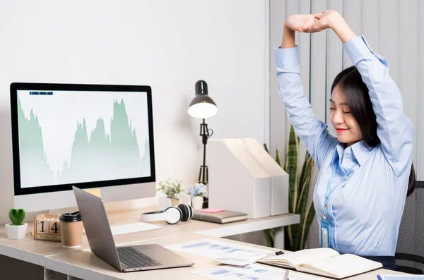 Asian female accountant is tired from working in a chair, stretching to relax and relax while working hard at the office.