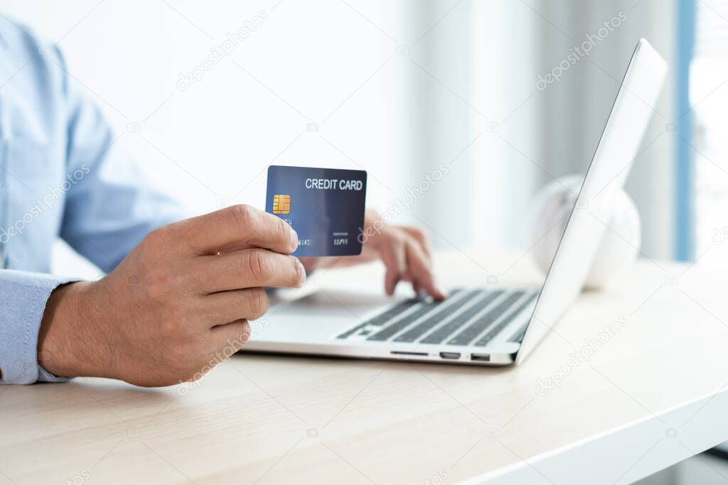 The businessman's hand is holding a credit card and using a laptop for online shopping and internet payment in the office.