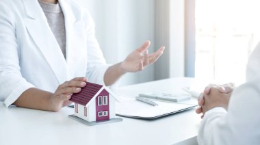 Ev modeli olan bir emlakçı ev sigortası almak için müşterilerle konuşuyor. Ev sigortası kavramı.