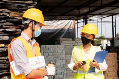 Erkek ve kadın mühendis veya mimarlardan oluşan bir ekip açık hava inşaat çalışmalarını inceliyor ve inceliyor.