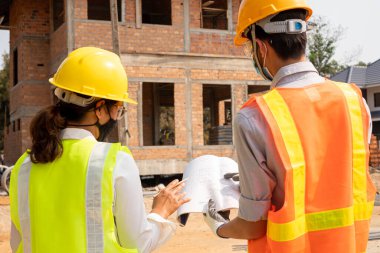 Erkek ve kadın mühendis veya mimarlardan oluşan bir ekip açık hava inşaat çalışmalarını inceliyor ve inceliyor.