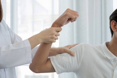 Kadın fizyoterapistler, dirsek yaralanması olan erkek hastalara rehabilitasyon merkezlerindeki hastaları muayene etmede yardımcı oluyorlar. Rehabilitasyon fizyoterapi konsepti.