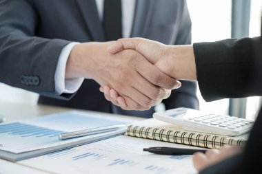 İki iş adamı el sıkışarak grafikler, finansal grafikler hakkında konuşuyor. Sonuçları gösteren planlama stratejileri analiz ediyor ve hesaplıyor. Ticari başarı oluşturma süreçleri..