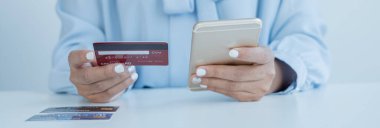 İş kadınının elinde bir kredi kartı var ve online alışveriş ve internet ödemeleri için akıllı telefon kullanıyor..
