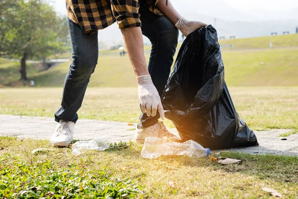 Man\'s hands pick up plastic bottles, put garbage in black garbage bags to clean up at parks, avoid pollution, be friendly to the environment and ecosystem.