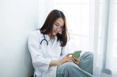 Oturan kadın doktorlar boş vakitlerinde hastanede akıllı telefon kullanmanın zevkini çıkarırlar..