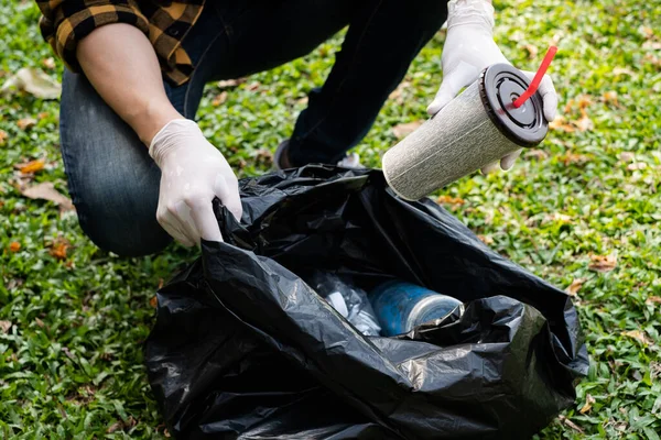 Man's hands pick up plastic bottles, put garbage in black garbage bags to clean up at parks, avoid pollution, be friendly to the environment and ecosystem.