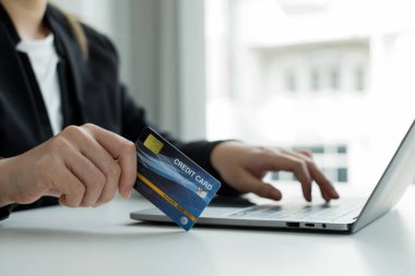 İş kadınlarının eli bir kredi kartı tutuyor ve online alışveriş ve internet ödemeleri için dizüstü bilgisayar kullanıyor.