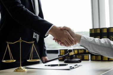 Hukuk bürosunda çalışan profesyonel erkek avukatların tokalaşması için teraziler, adalet terazileri, yargıç tokmağı ve dava belgeleri var. Hukuk ve adalet kavramları.