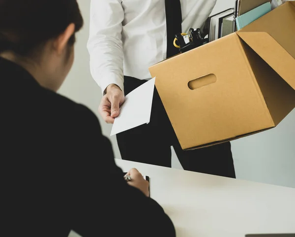 Desperately fired man office worker employee hands her employer her resignation letter and packs her belongings in a cardboard box concept dismissal and unemployment.