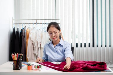 Tekstil aksesuarları ve girişimci tasarımcı çizimleriyle genç ve güzel Asyalı moda terzisi stüdyoda yaratıcı fikirler için dizüstü bilgisayarı olan parlak renklerle dolu..