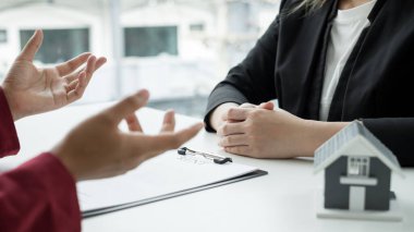 Ev modeli olan bir emlakçı ev sigortası almak için müşterilerle konuşuyor. Gayrimenkul Ev Sigortası.