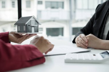Ev modeli olan bir emlakçı ev sigortası almak için müşterilerle konuşuyor. Gayrimenkul Ev Sigortası.