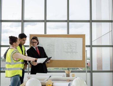 Erkek ve kadın mühendisler ve mimarlardan oluşan bir ekip, çalışma ekibi, inşaat planlarını tartışıyor ve çiziyor, baskı yapıyor, inşaat alanlarında yazıyor..