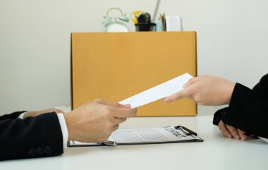 Desperately fired female office worker employee hands her employer her resignation letter and packs her belongings in a cardboard box concept dismissal and unemployment.