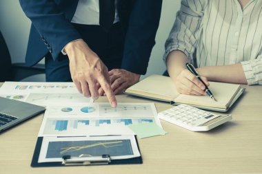 İki iş lideri çizelgeler, finansal grafikler hakkında konuşuyor. Sonuçları gösteren planlama stratejilerini analiz ediyor ve hesaplıyor. Ticari başarı oluşturma süreçlerini de..