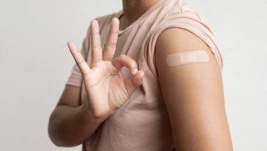 Asyalı kadın Covid-19 'a karşı aşılandıktan sonra omzunda alçı olduğunu gösteriyor. Coronavirus aşı kampanyası konsepti.