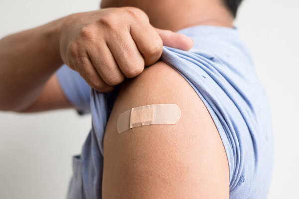 Asian man shows plaster on her shoulder after being vaccinated against Covid-19. Coronavirus vaccination campaign concept.