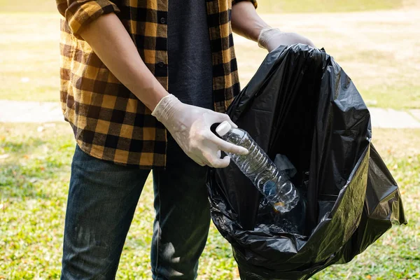 Man\'s hands pick up plastic bottles, put garbage in black garbage bags to clean up at parks, avoid pollution, be friendly to the environment and ecosystem.