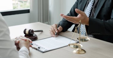 Bir erkek avukat ya da yargıç müvekkillerine adalet ve kovuşturma konusunda danışmanlık yapıyor. Teraziler, yargıç tokmağı, yasal belgeler, yasal hizmetler kavramı..