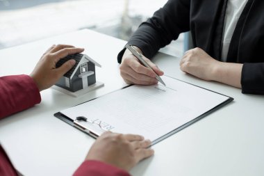 Ev modeli olan bir emlakçı ev sigortası almak için müşterilerle konuşuyor. Gayrimenkul Ev Sigortası.