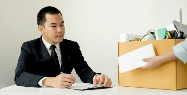 Desperately fired female office worker employee hands her employer her resignation letter and packs her belongings in a cardboard box concept dismissal and unemployment.