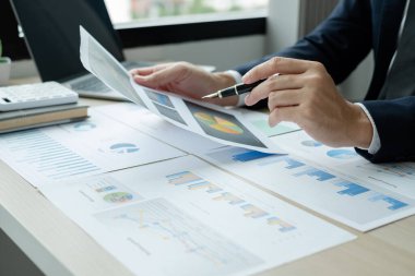 İş adamının eli masalarında oturup yatırımlarıyla ilgili sonuçları gösteren finansal grafikleri hesaplıyor, başarılı bir iş büyüme süreci planlıyor.