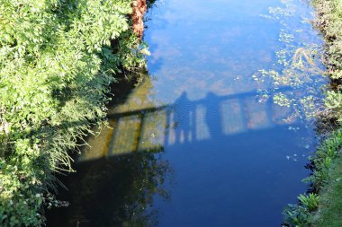 Köprüde dikilip bir kanala bakan bir kadın ve erkeğin gölgesi..