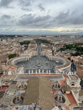Vatikan Şehri, İtalya, 10 Kasım 2023. Aziz Peter Meydanı 'nın panoramik manzarası Bazilika' nın kubbesinden, Bernini 'nin sütununun uzayı, merkezi dikilitaşı ve Roma şehrinin dramatik, bulutlu bir gökyüzü altında uzanmasıyla.