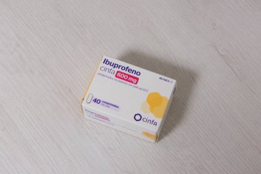 Pamplona, İspanya - 12 Şubat 2026. Görüntü, açık ahşap bir yüzeye yerleştirilmiş bir ilaç kutusunu gösteriyor. İçinde Cinfa Ibuprofen 600 mg film kaplı tabletler var. Paket beyaz, mor ve sarı detaylarla dolu.