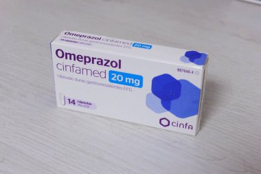 Pamplona, İspanya - 12 Şubat 2026. Bir kutu Omeprazole Cinfamed 20 mg hafif ahşap bir yüzeye yerleştirilir. Paket mor ve mavi detaylarla beyaz ve oral yönetim için 14 gastro dirençli sert kapsül içerdiğini gösteriyor.