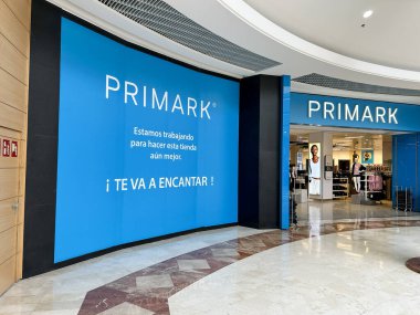 Pamplona, İspanya, 23 Şubat 2026. Mağazayı geliştirmek için çalıştıklarını belirten bir reklam mesajı içeren büyük mavi duvarlı bir alışveriş merkezi içindeki bir Primark mağazası, mavi arka planda beyaz logo göze çarpıyor.,