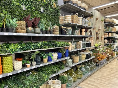 Pamplona, İspanya - 28 Şubat 2026. Bir Conforama ev dekorasyonu mağazası. Raflar yapay bitkiler, saksılar, cam vazolar, hasır sepetler ve çiçeklerle dolu. Ürünler boyut ve malzemeye göre düzenlenir, yeşil, bej.