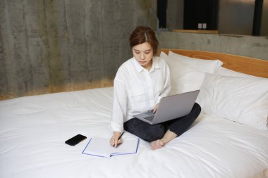 Asyalı iş kadını evinde, yatağında çalışıyor.