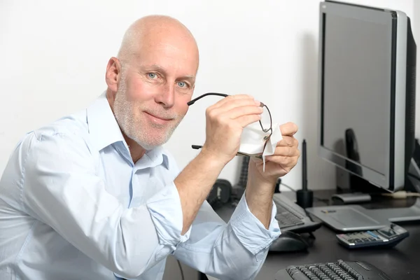 Middle-aged man cleans his glasses in his office — Stock Photo, Image