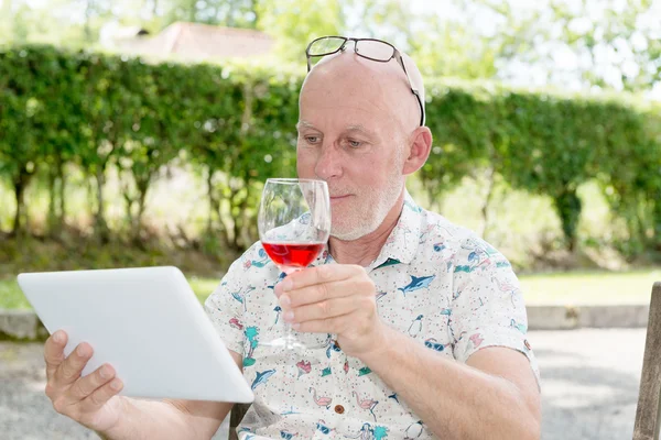 Hombre con una tableta y una copa de vino tinto en el jardín — Foto de Stock