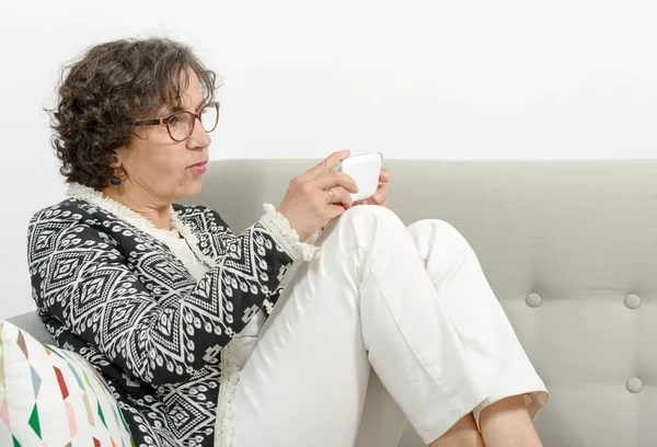 Mujer madura en el sofá con un teléfono — Foto de Stock