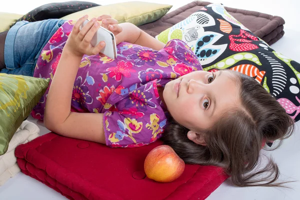 Schoolmeisje met een mobiele telefoon, liggend op de vloer — Stockfoto