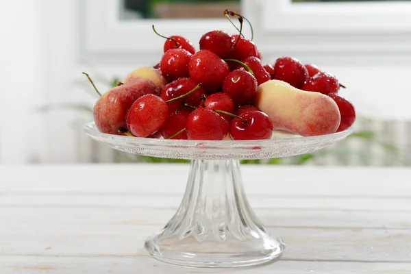 Cherries and peaches in a glass cup — Stock Photo, Image