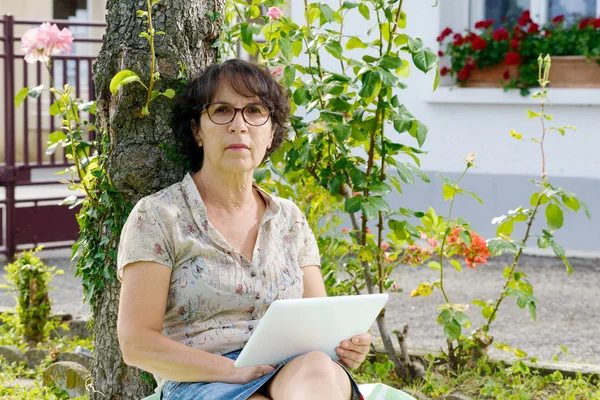 Mulher madura sentada com um tablet no jardim — Fotografia de Stock