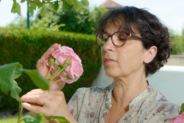 Zralá žena vonící růže její zahrada — Stock fotografie